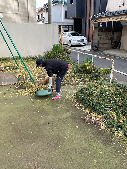 落ち葉を大きなちりとりで集める女性