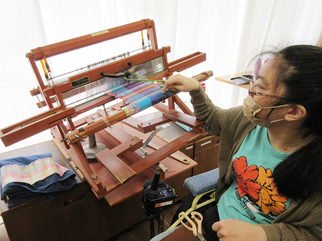 木製の手動織機と、それを操作する女性